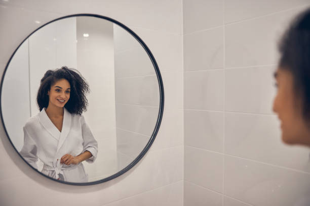 sonriendo mujer bonita de pie en un baño - round mirror fotografías e imágenes de stock