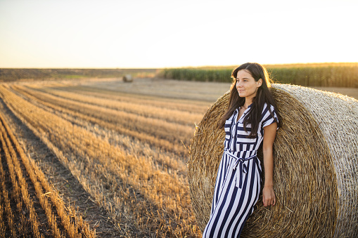 Fashion woman standing on harvested field with straw bales