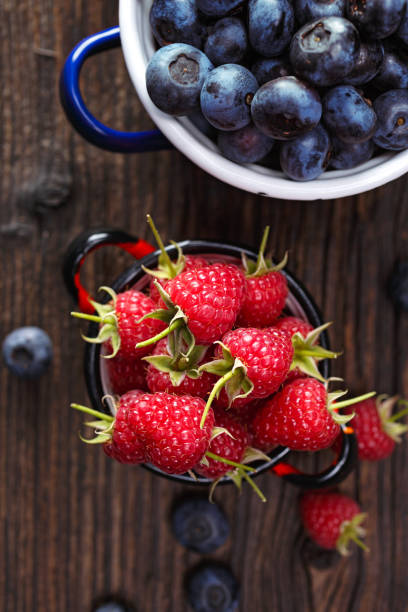 istock Fresh raspberries and blueberries in a enameled pots on a wooden rustic table 1222389578