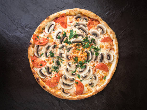 istock Pizza with mushrooms and tomatoes on a rough dark stone surface top view 1222392073