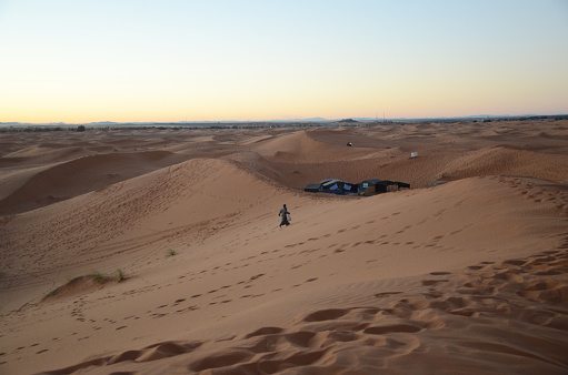 Sunset time at Merzouga with a man walking back to his tent. Merzouga is a small Moroccan town in the Sahara Desert, near the Algerian border.