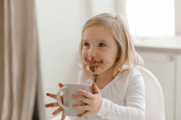 istock A contented smiling baby smudged with chocolate sits at a table with a mug in her hands. 1222396330