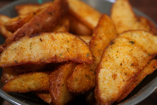 Stock photo showing a pile of freshly cooked, homemade, potato wedges in a crispy coating in a green dish.