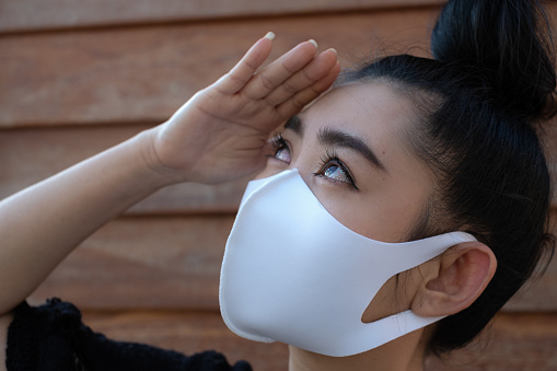 Close up beautiful young Asia woman putting on a medical mask to protect from airborne respiratory diseases as the flu dust and smog at wall wood background, Women safety virus infection concept