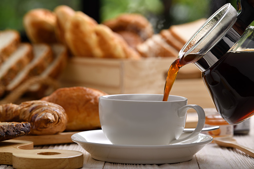Pouring coffee with smoke on a cup with breads or bun, croissant and bakery on white wooden table photo