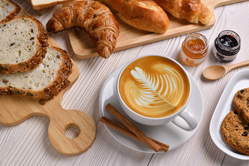 Top view of cup of coffee latte with breads or bun, croissant and bakery on white wooden table