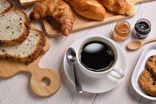 Top view of cup of coffee with breads or bun, croissant and bakery on white wooden table