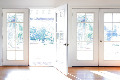 A door is open in a brightly lit room full of French doors and hardwood flooring.