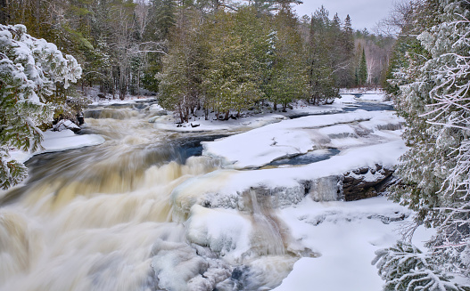 In winter after a fresh snowfall, the rushing water of Egan Chutes waterfall near Bancroft, runs between the snow covered rocky tree lined shores.