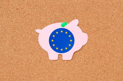 Paper piggy bank with european union flag hanging from cork board