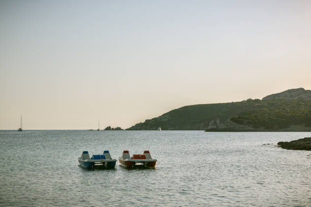 zwei tretboote schwimmen am abend in der nähe der küste in der nähe von capo testa auf sardinien auf dem wasser - pedal boat stock-fotos und bilder