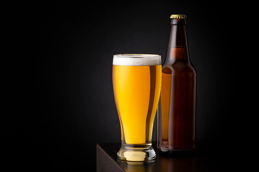 Glass of cold pale beer and a beer bottle placed on a bar counter with copy space