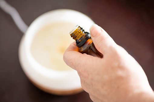 This is a photograph of a woman’s hand putting essential oil into a plugged in diffuser viewed from above during lockdown at home in Miami, Florida.