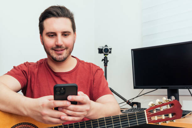 istock Blogger checking his phone before giving the guitar lesson from his home recording studio 1222425534