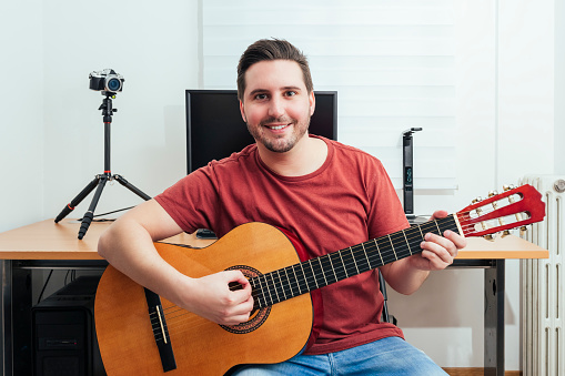 Portrait of a blogger playing guitar from his home recording studio. Learning online concept.