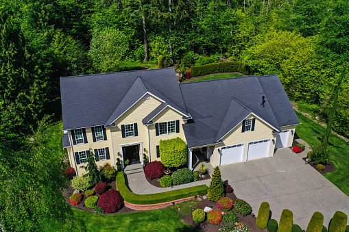 Aerial view of a yellow modern American craftsman home with lush landscaping, set among a forest of trees