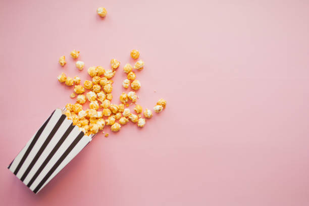 istock Popcorn in paper bag scattered on pink background top view 1222429214