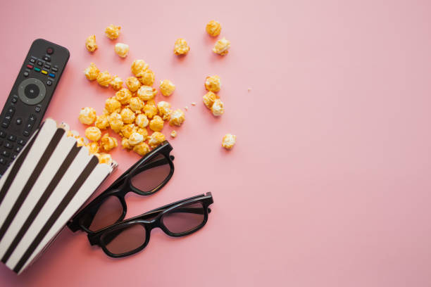 two black 3d glasses lie next to a black and white papper striped box of popcorn and tv remote control - remote television movie box imagens e fotografias de stock