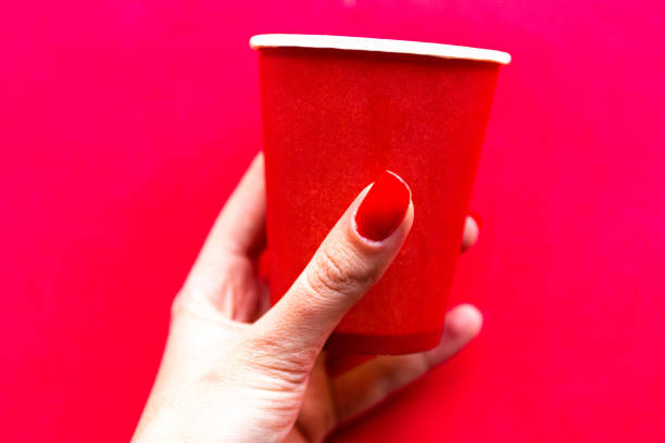 istock Womans hand with red nails holds red take away coffee cup on bright red background 1222432322