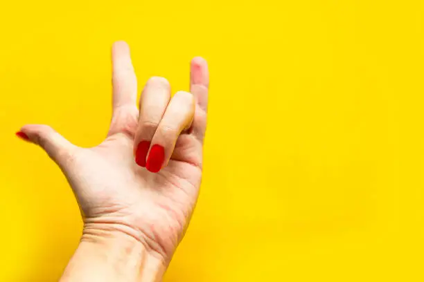 Woman's hand shows the rock sign over bright yellow background. Top view, copy space for the text