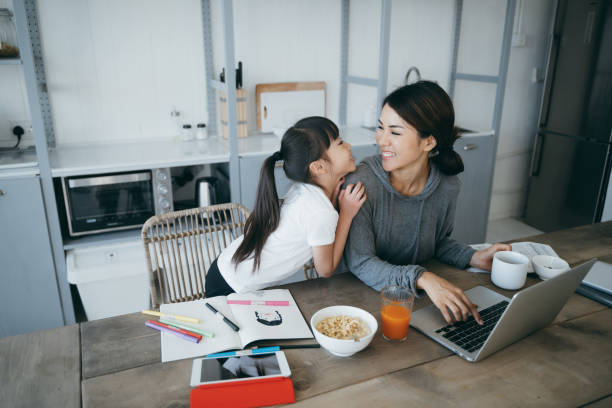 Young Asian mother working from home on a laptop while little daughter is studying from home with a digital tablet. They are enjoying the time together Young Asian mother working from home on a laptop while little daughter is studying from home with a digital tablet. They are enjoying the time together epidemiology student stock pictures, royalty-free photos & images