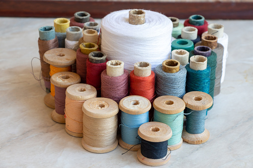 Spools of thread of different sizes with threads of different colors stands on the table. Theme of hobby at home.