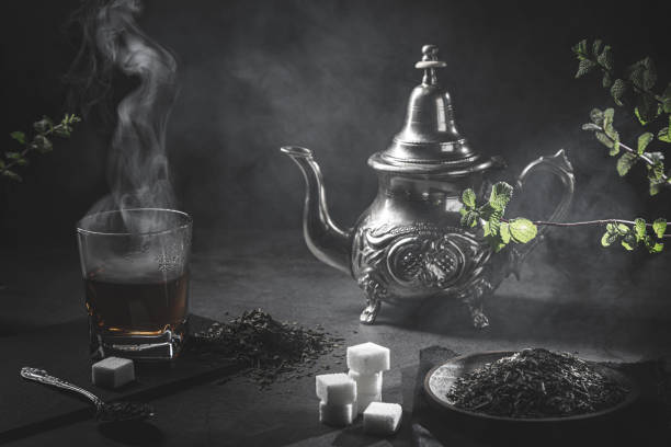 teiera tradizionale marocchina, con una tazza fumante di tè, zucchero e menta, in un'atmosfera nera fumosa. concetto di tè marocchino. - te bevanda calda foto e immagini stock