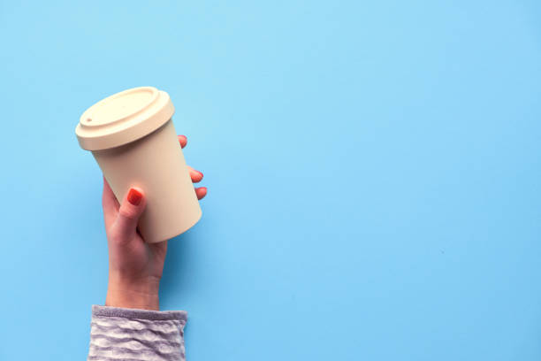 istock Bamboo coffee cup, keep cup or travel mug in female hand on blue mint background. Creative flat lay, top view image with copy-space. Trendy zero waste concept with eco friendly travel cup. 1222442391