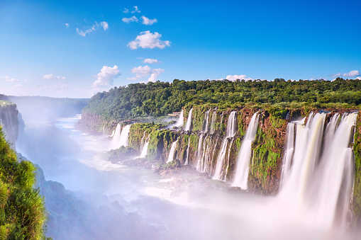 Iguazu waterfalls in Argentina, panoramic view of the valley with steam from Devil's Mouth on a bright day with blue sky