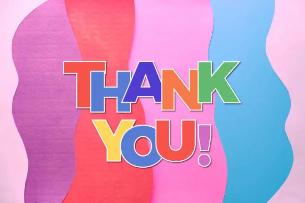 Thank you text in rainbow letters on layered colorful abstract paper background. Thank you doctors, nurses and essential key workers taking care of our life and well being during Covid-19 pandemics!