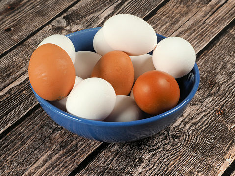 Chicken eggs in a ceramic bowl on dark wooden background