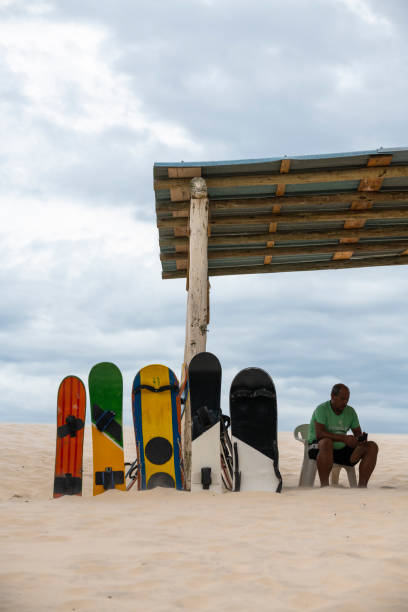 Sandboard rental at Joaquina sand dunes in Florianopolis, Brazil A man rents boards at the sand dunes of Joaquina in Florianópolis, Brazil. The dunes are a popular place for sandboarding. (April 5, 2019) joaquina beach in florianopolis santa catarina brazil stock pictures, royalty-free photos & images