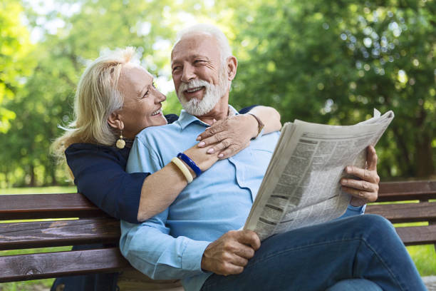 lächelnde senior paar entspannen im freien lesen zeitung im park - senior adult women park bench 70s stock-fotos und bilder