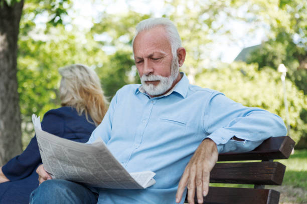 senior paar entspannen im freien lesen zeitung im park zurück nach hinten - senior adult women park bench 70s stock-fotos und bilder