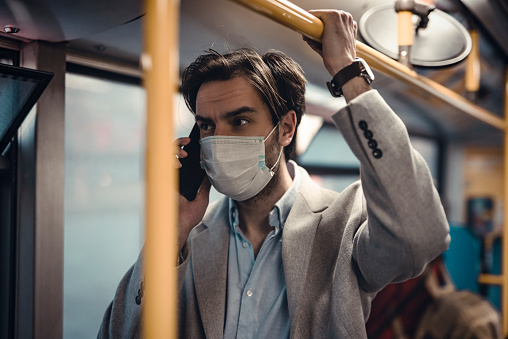 Depressing scene of a young man wearing a surgical mask during the coronavirus outbreak in Europe, talking on his mobile phone. Public transportation curfew.
