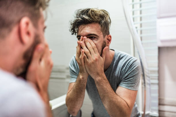 How am I going to face this day? Shot of a young man standing in front of the bathroom mirror looking exhausted. man regret stock pictures, royalty-free photos & images