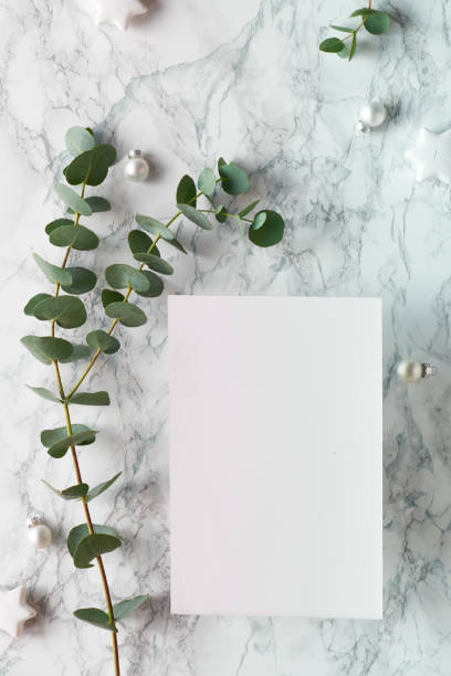 istock Christmas frame with fresh eucalyptus twigs and white trinkets with black stars. Flat lay marble background, blank paper page with copy-space, space for text.. 1222457890