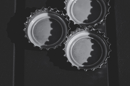 Three bottle tops beside one another, resting on a painted wooden plank.  Black and white.  Matte effect.