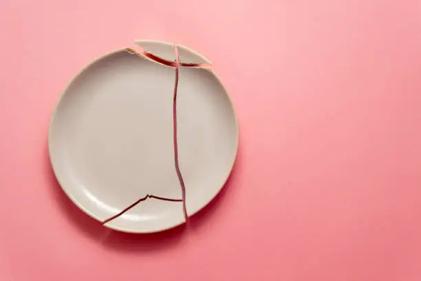 Photo of broken white plate on pink background, concept visual