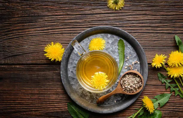 Herbal drink for liver detox, dandelion root tea in a glass cup decorated with fresh flowers on a rustic wooden background with copy space