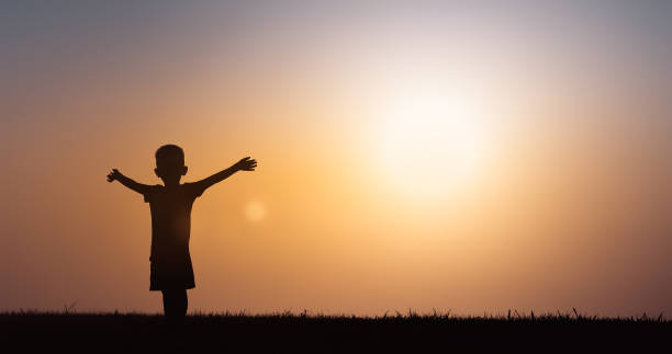 istock Happy little boy, child feeling free with arms up facing sunset sky. 1222468011