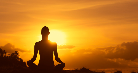 Young woman sitting in lotus position and does yoga for healthy lifestyle on ocean beach. Female performing sports exercises to restore strength and spirit. Yoga position on seashore