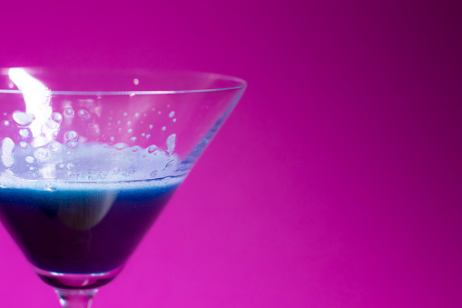 blue liquid in a cocktail martini glass on a pink background