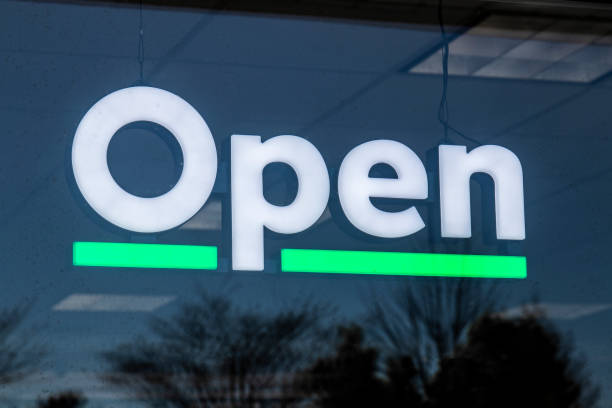 Open sign in white text and green light underline hanging in a storefront window.