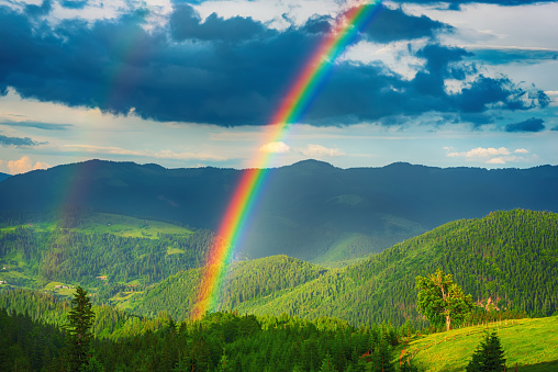 Beautiful mountain valley with green hills and huge rainbow in summer. Natural outdoor travel background. Carpatians, Ukraine