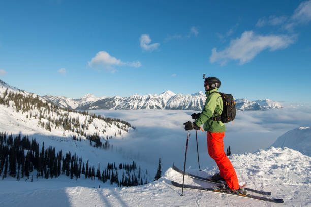 альпийский лыжник отдыхает над туманным берегом, горами и д�олиной - skiing british columbia sports helmet tree стоковые фото и изображения