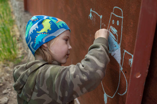 Un garçon dessine un robot sur un mur rouillé. - Photo