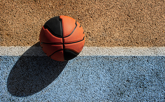 Basketball ball in a blue and yellow street court on a sunny day. Top view. Copy space.