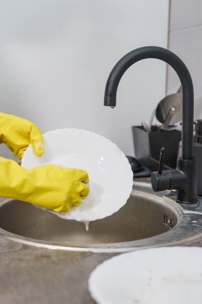 istock Close up on yellow rubber protective gloves on female unknown woman woman's hands manually washing plates dishes in the kitchen by the sink side view at home by the tap water in day side view 1222488925