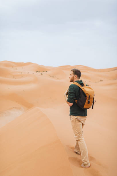 istock Man backpacker travel in Morocco, Sahara desert.  Explore african nature, sand dunes around. View from behind. 1222498115